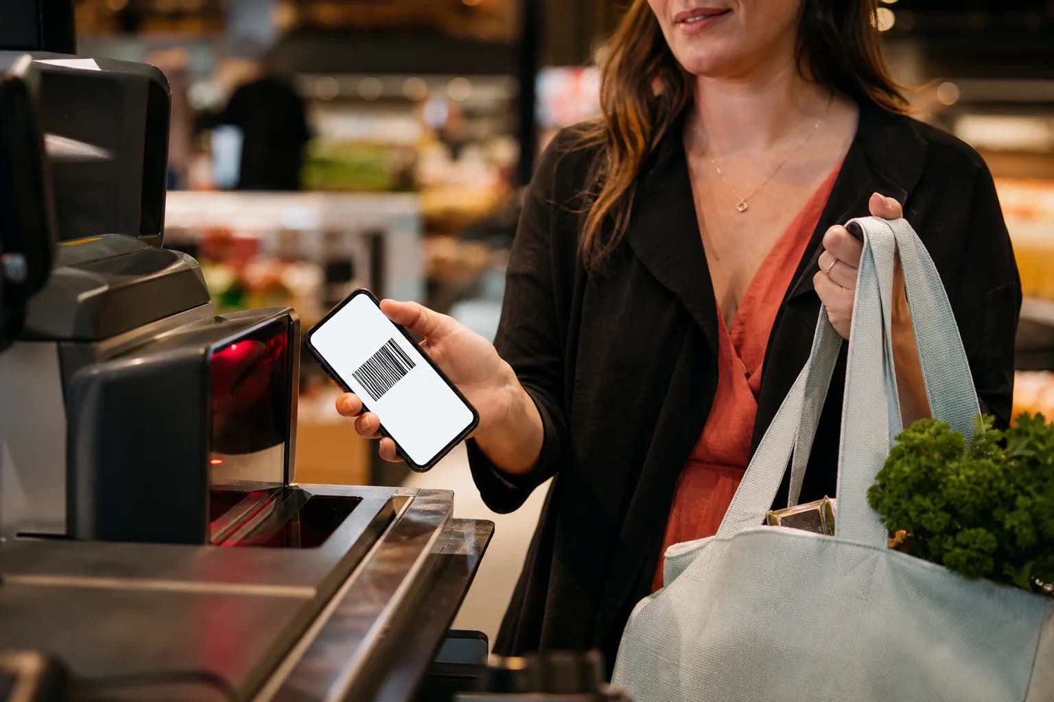 Shopper holding a loyalty barcode on their phone at a grocery scanner