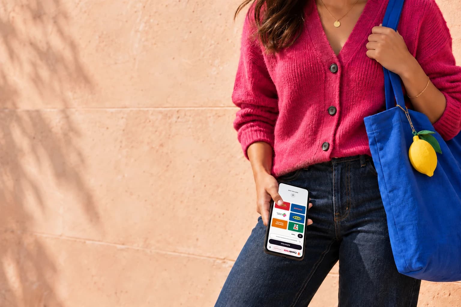 A shopper in a pink cardigan with a blue tote and phone