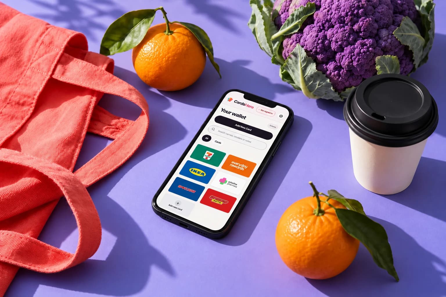 A colourful shopping bag, coffee, groceries and a phone on a lilac surface